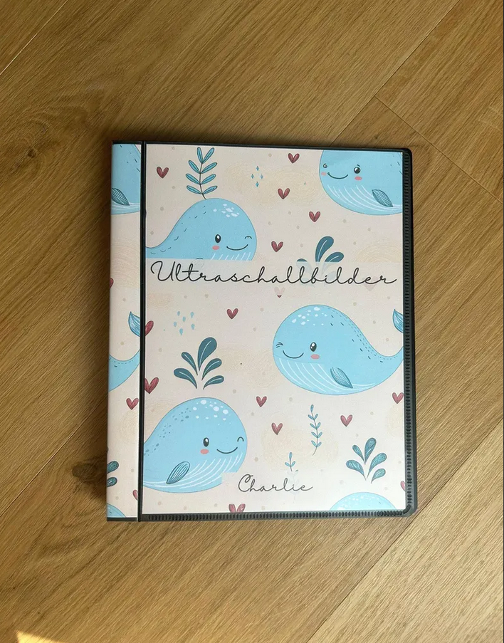Personalisierbares Ultraschallalbum "Wal" mit Aufschrift Ultraschallbilder und Name "Charlie" auf Holztisch