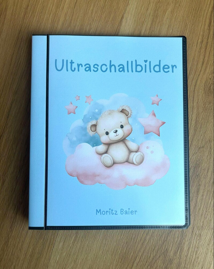 Personalisierbares Ultraschallalbum, blau mit Teddybär mit Aufschrift Ultraschallbilder und Name Moritz auf Holztisch