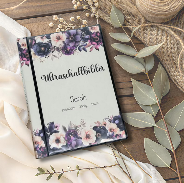 Personalisierbares Ultraschallalbum mit lila Blumen Design mit Aufschrift Ultraschallbilder und Name Sarah auf Holztisch