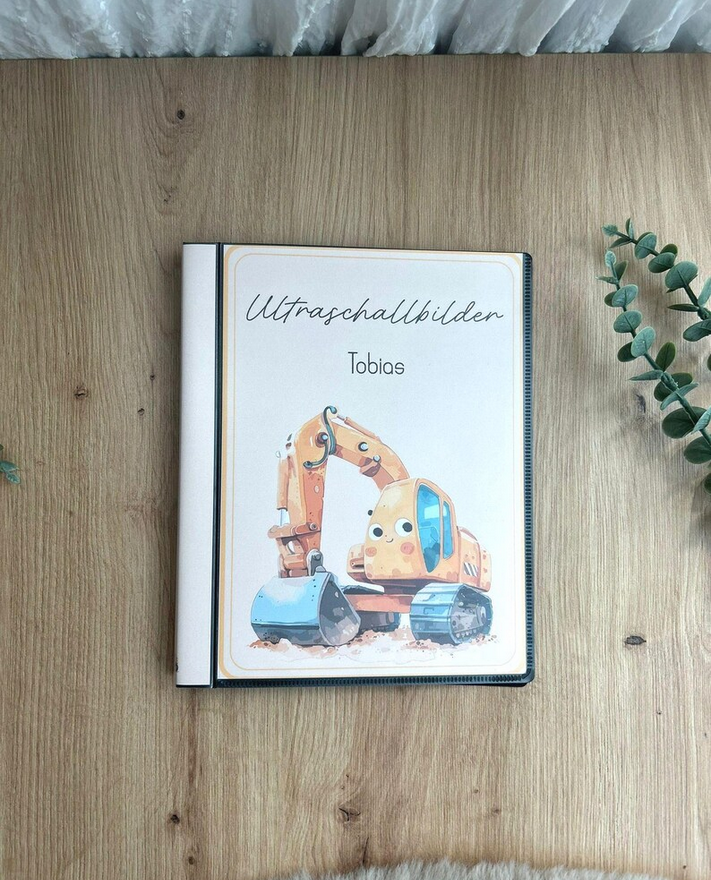 Personalisierbares Ultraschallalbum Bagger mit Aufschrift Ultraschallbilder und Name Tobias auf Holztisch