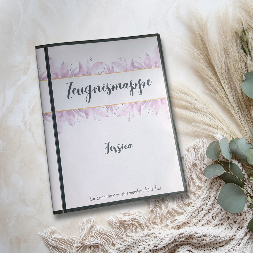 Die stabile Hardcover Zeugnismappe mit dem lila Blumenrand liegt auf dem Tisch und ist mit dem Namen des Kindes personalisierbar