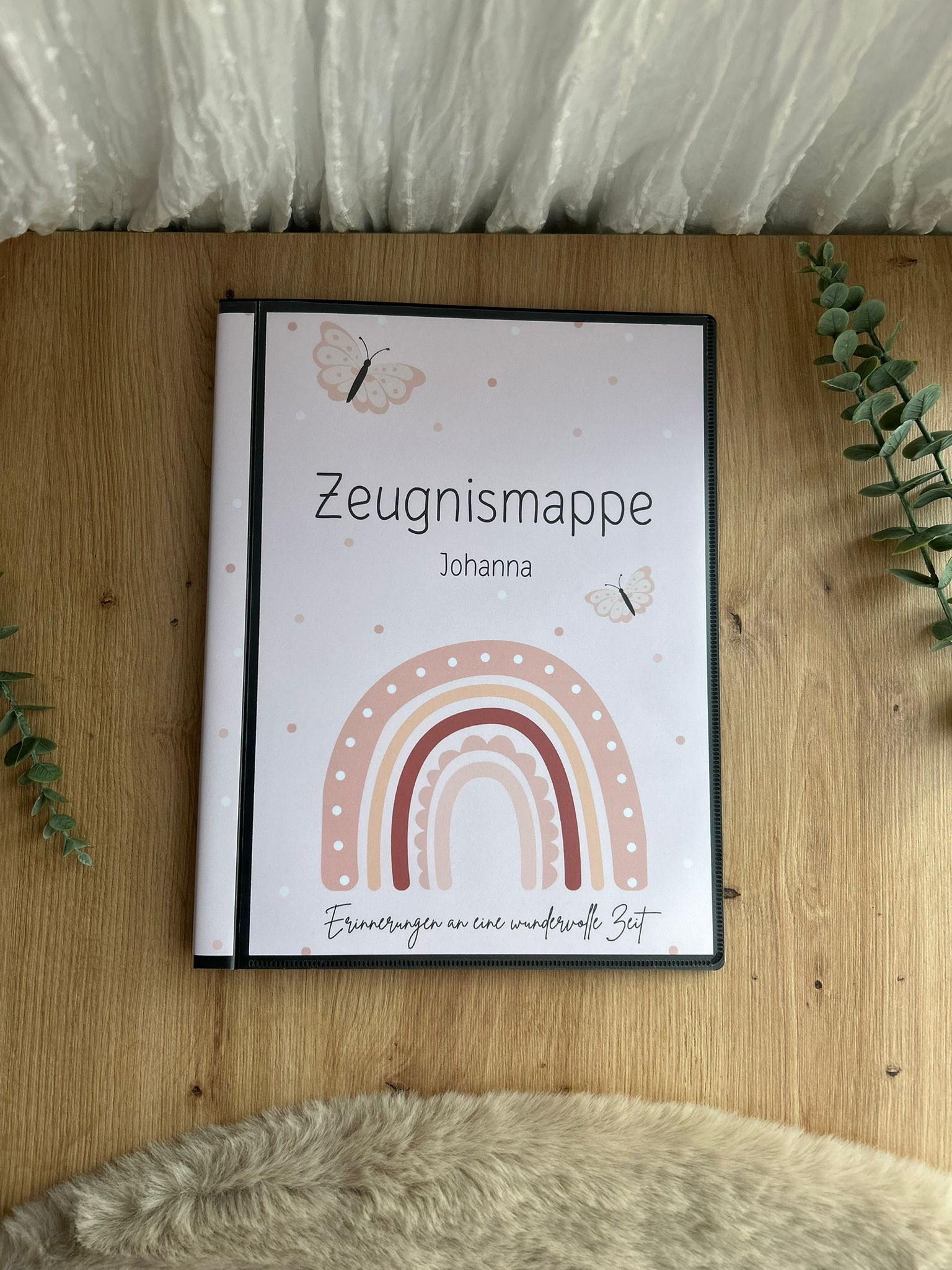 Zeugnismappe Johanna mit Regenbogen-Motiv und Schmetterlingen auf Holztisch – stabiles Hardcover, bedruckter Seiteneinband